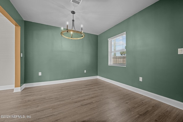 spare room featuring wood-type flooring and a notable chandelier