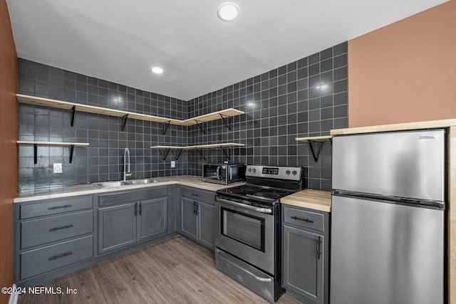 kitchen with sink, decorative backsplash, gray cabinets, light wood-type flooring, and appliances with stainless steel finishes