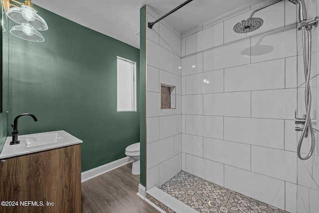 bathroom with hardwood / wood-style flooring, vanity, toilet, and a tile shower