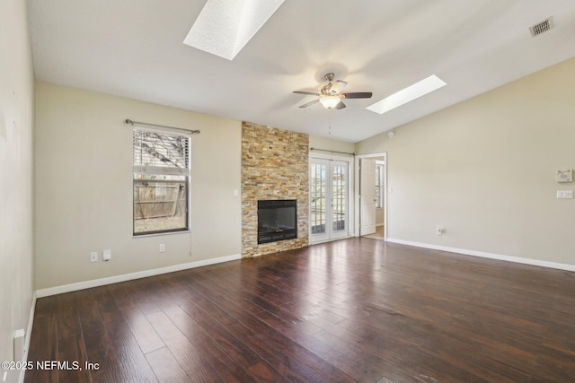 unfurnished living room featuring ceiling fan, dark hardwood / wood-style floors, lofted ceiling with skylight, and a fireplace