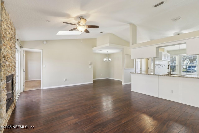 unfurnished living room with dark hardwood / wood-style flooring, a fireplace, ceiling fan with notable chandelier, and vaulted ceiling with skylight