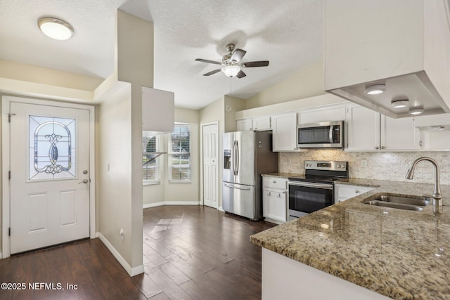 kitchen with sink, stainless steel appliances, vaulted ceiling, stone countertops, and white cabinets