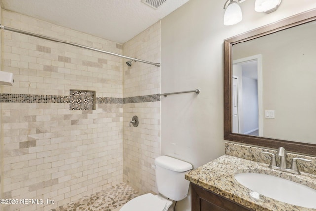 bathroom with tiled shower, vanity, a textured ceiling, and toilet