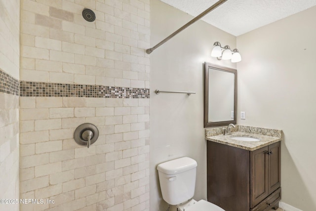 bathroom featuring toilet, vanity, a textured ceiling, and tiled shower