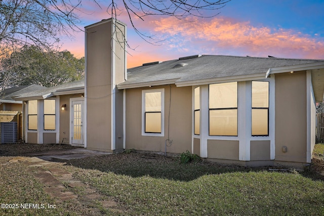 back house at dusk with a lawn and central AC