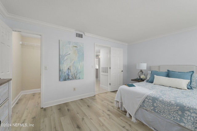 bedroom featuring a walk in closet, crown molding, a closet, and light hardwood / wood-style floors