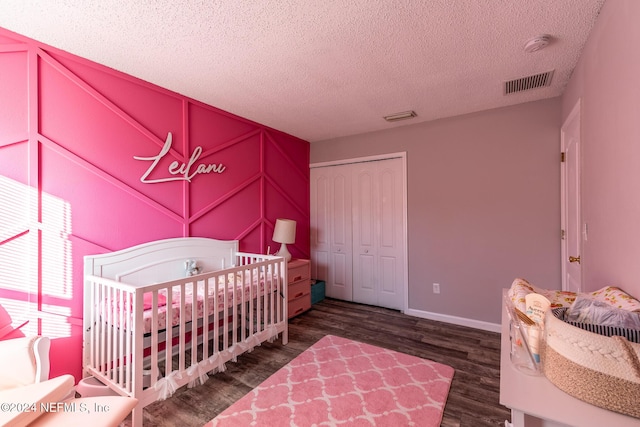 bedroom featuring dark wood-type flooring, a closet, a nursery area, and a textured ceiling