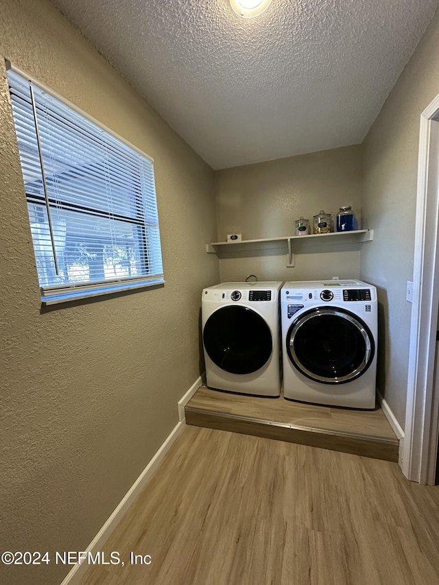 clothes washing area with light hardwood / wood-style flooring, washer and dryer, and a textured ceiling