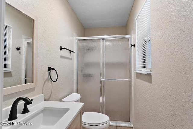 bathroom with a textured ceiling, vanity, toilet, and a shower with door