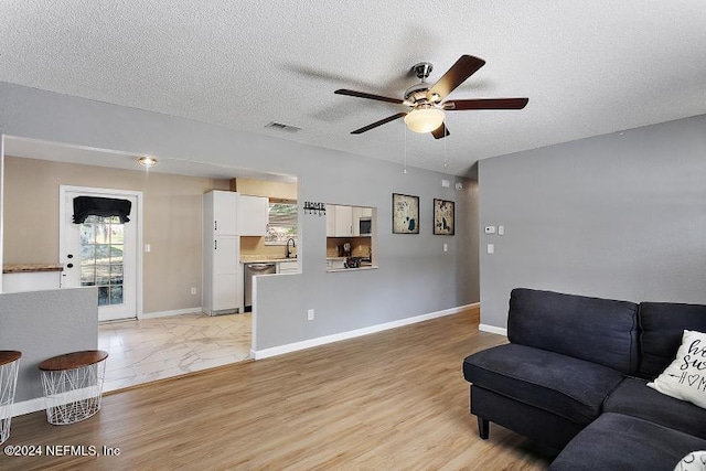 living room featuring ceiling fan, plenty of natural light, a textured ceiling, and light wood-type flooring