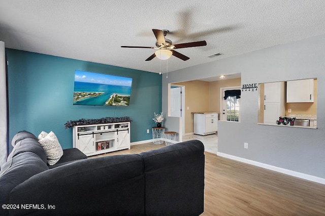 living room with ceiling fan, light wood-type flooring, and a textured ceiling