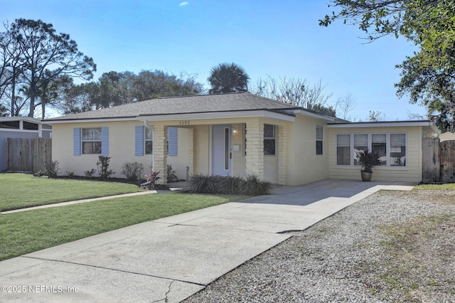 ranch-style house featuring a shingled roof, fence, driveway, and a front lawn