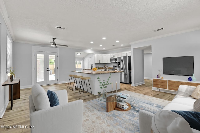 living room featuring french doors, a textured ceiling, light hardwood / wood-style flooring, and ornamental molding