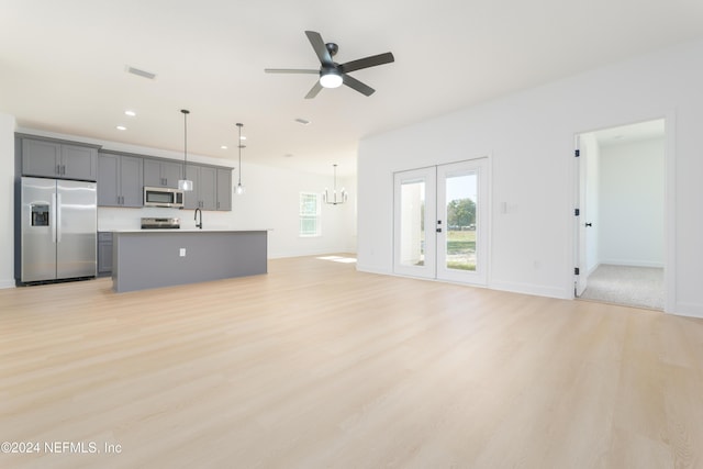 unfurnished living room with ceiling fan with notable chandelier, light wood-type flooring, sink, and french doors