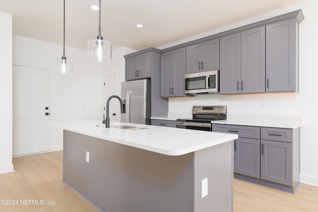 kitchen with decorative light fixtures, stainless steel appliances, a kitchen island with sink, and light hardwood / wood-style floors