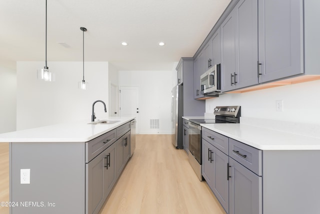 kitchen featuring sink, hanging light fixtures, light hardwood / wood-style floors, a kitchen island with sink, and appliances with stainless steel finishes