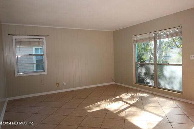 spare room with light tile patterned floors, wooden walls, and ornamental molding