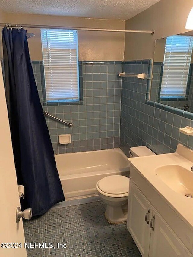 full bathroom featuring vanity, tile patterned floors, toilet, a textured ceiling, and tile walls