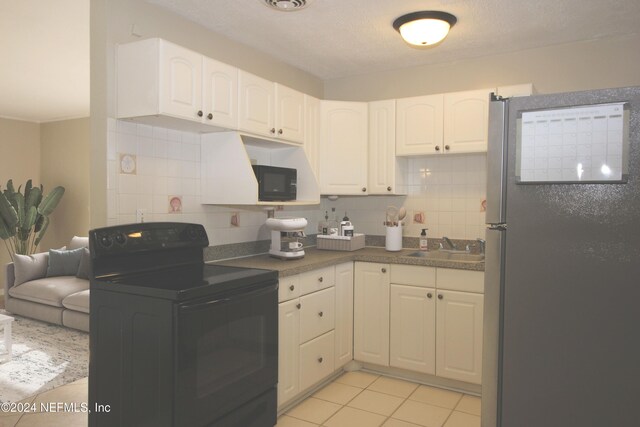 kitchen with tasteful backsplash, white cabinetry, stainless steel refrigerator, and black / electric stove