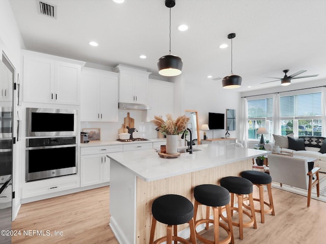 kitchen featuring white cabinets, hanging light fixtures, ceiling fan, gas stovetop, and an island with sink