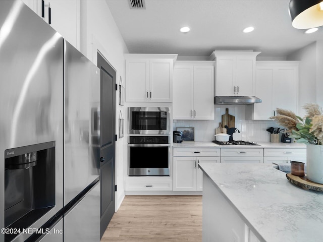 kitchen featuring light stone countertops, stainless steel appliances, backsplash, white cabinets, and light wood-type flooring