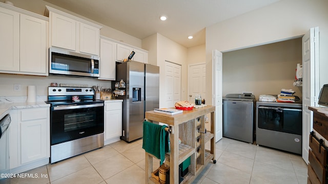 kitchen featuring light tile patterned floors, stainless steel appliances, white cabinetry, and washer and clothes dryer