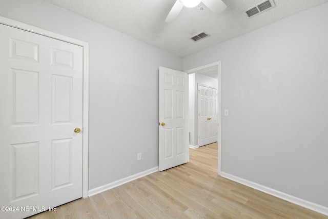 unfurnished bedroom featuring ceiling fan, a closet, light hardwood / wood-style floors, and a textured ceiling