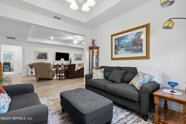 living room with a tray ceiling, wood-type flooring, and ceiling fan with notable chandelier