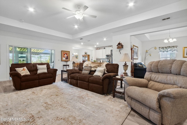 living room featuring ceiling fan with notable chandelier, light wood-type flooring, and a tray ceiling