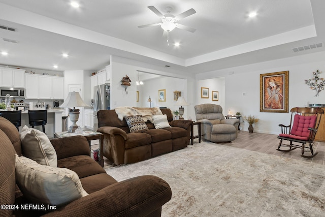 living room with light wood-type flooring, a tray ceiling, and ceiling fan