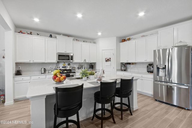 kitchen with a center island with sink, white cabinets, light wood-type flooring, and stainless steel appliances