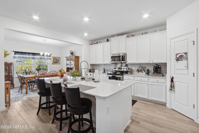 kitchen featuring white cabinets, appliances with stainless steel finishes, light hardwood / wood-style floors, and a kitchen island with sink