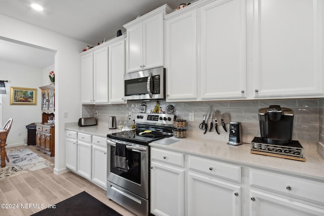 kitchen featuring white cabinetry, light stone countertops, tasteful backsplash, light hardwood / wood-style flooring, and appliances with stainless steel finishes