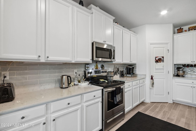 kitchen featuring backsplash, white cabinets, light wood-type flooring, light stone counters, and stainless steel appliances