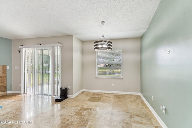 unfurnished dining area featuring a notable chandelier, a healthy amount of sunlight, and a textured ceiling