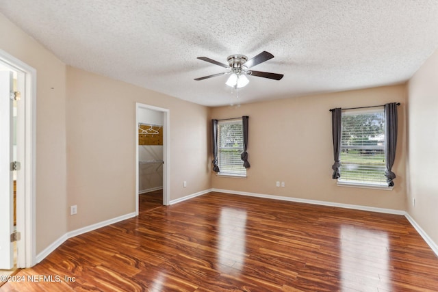 unfurnished bedroom with ceiling fan, dark hardwood / wood-style flooring, a spacious closet, and multiple windows