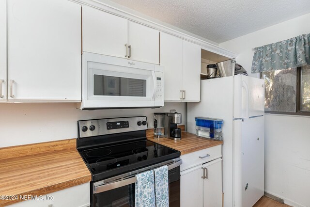 kitchen with butcher block counters, light hardwood / wood-style floors, a textured ceiling, white appliances, and white cabinets