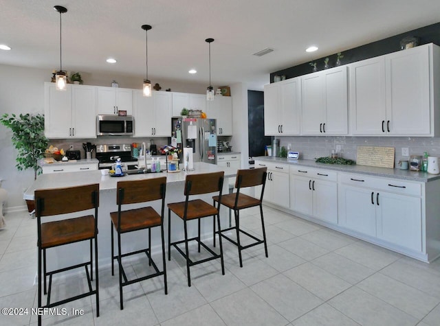 kitchen with decorative light fixtures, stainless steel appliances, white cabinetry, and an island with sink