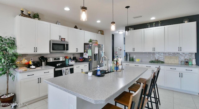 kitchen featuring appliances with stainless steel finishes, tasteful backsplash, a center island with sink, white cabinetry, and a breakfast bar area