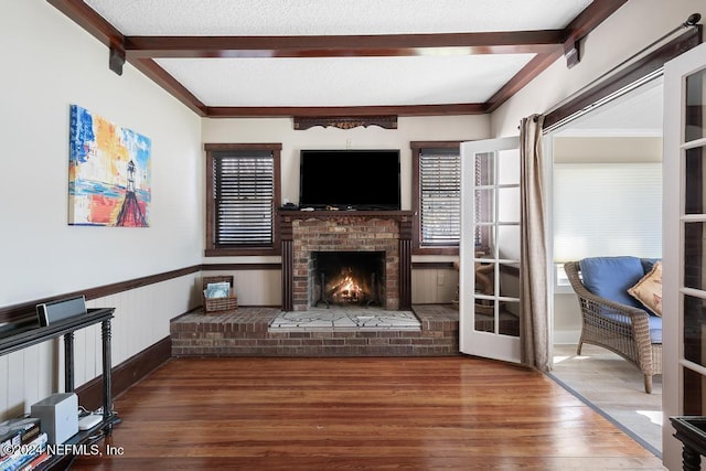 living room with a fireplace, wood-type flooring, crown molding, and beamed ceiling