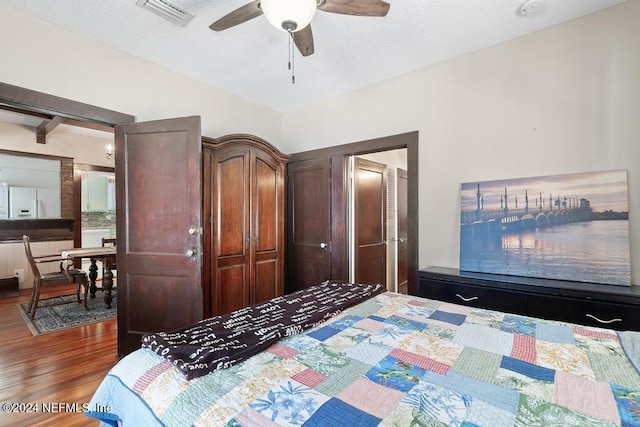 bedroom with dark hardwood / wood-style flooring, a textured ceiling, ceiling fan, white fridge with ice dispenser, and a closet