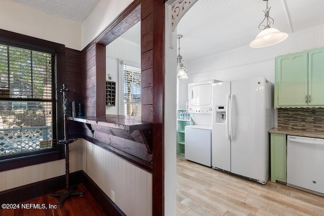 kitchen with a wealth of natural light, white appliances, stacked washer and dryer, and hanging light fixtures