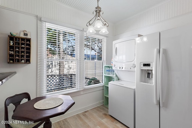 laundry area with an inviting chandelier, stacked washing maching and dryer, and light wood-type flooring