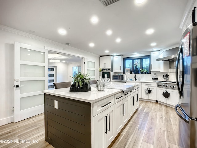 kitchen featuring white cabinets, wall chimney exhaust hood, a kitchen island, and stainless steel appliances