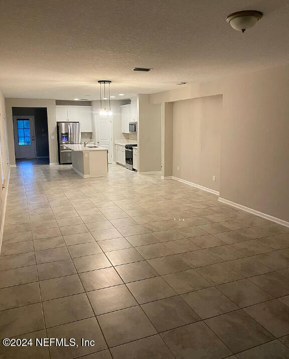 unfurnished living room featuring sink, light tile patterned floors, and a textured ceiling