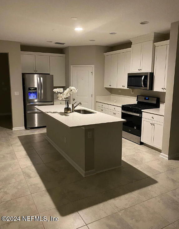 kitchen with white cabinets, appliances with stainless steel finishes, a center island with sink, and sink