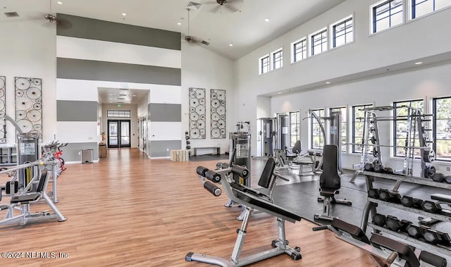 exercise room featuring ceiling fan, light hardwood / wood-style flooring, and a towering ceiling