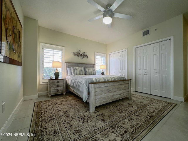 bedroom featuring ceiling fan, light tile patterned flooring, multiple closets, and multiple windows