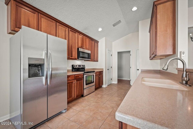 kitchen featuring a textured ceiling, stainless steel appliances, vaulted ceiling, sink, and light tile patterned floors