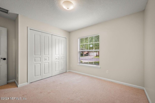 unfurnished bedroom with a textured ceiling, light carpet, and a closet